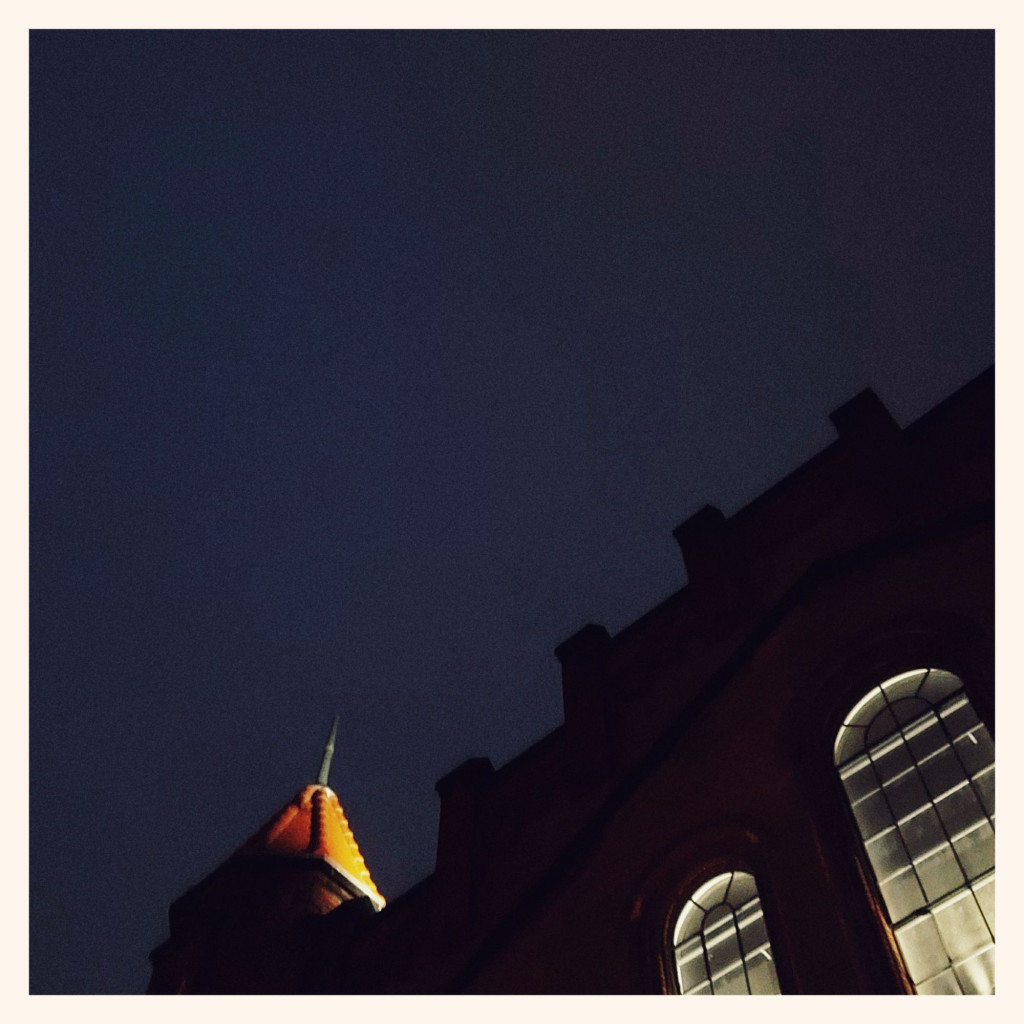 Shapeless nightsky above an old facade. Bright windows, slightly lit small tower.