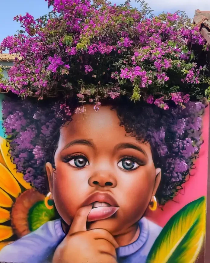 A captivating mural by Fábio Gomes Trindade in Goiás, Brazil, featuring the portrait of a young Black girl with a thoughtful expression, her finger resting on her lips. Her afro blends beautifully with a cascade of magenta bougainvillea flowers from a tree above. The artwork is enriched with vibrant details, including a sunflower and green leaf in the background, emphasizing the connection between nature and art.