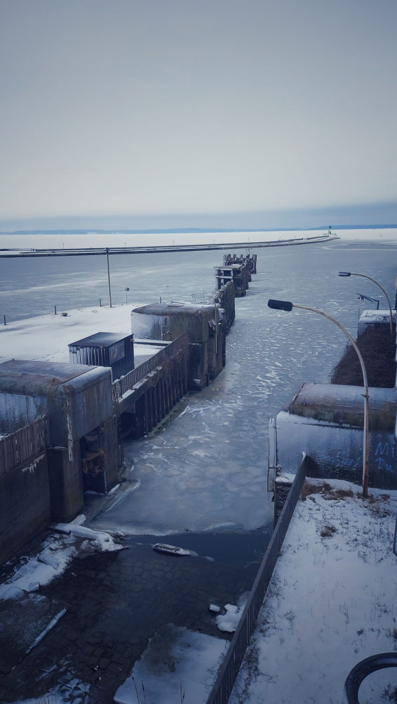 An abandoned port slightly iced. A quay wall and a lighthouse in the back.