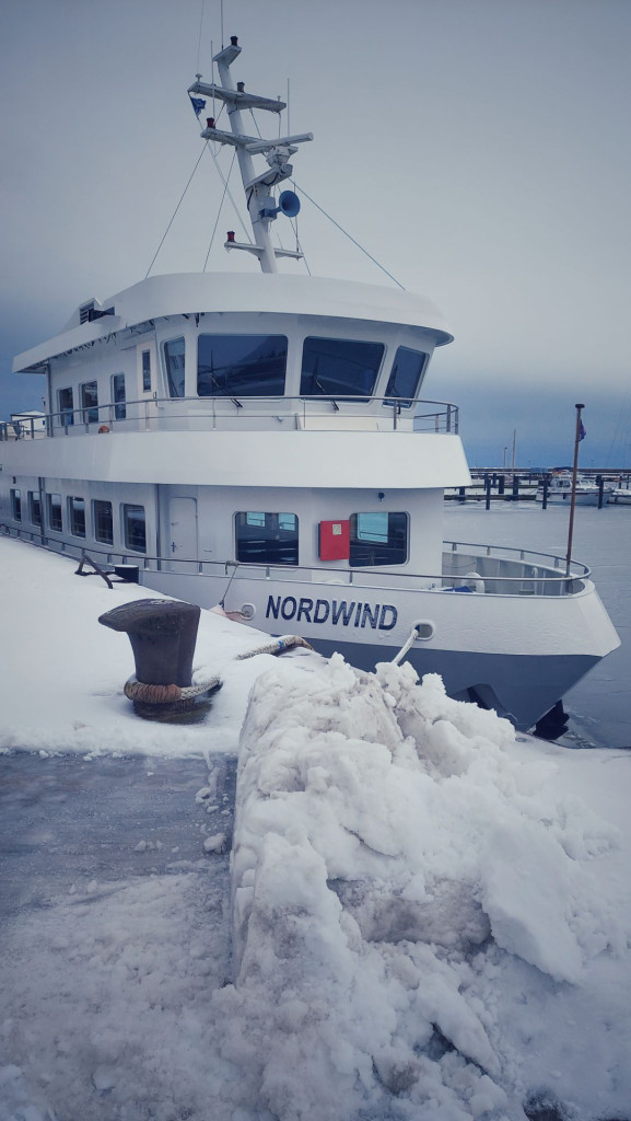 A ship named Nordwind resting on a quay, near a heap of snow.