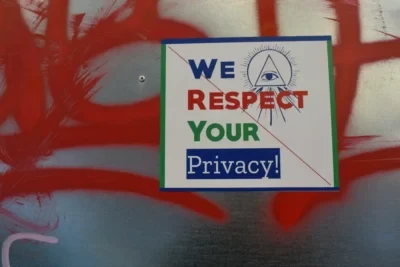 Sign with an eye symbol and text "WE RESPECT YOUR Privacy!" against a metal surface with red graffiti background.