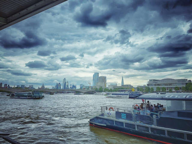 Thames with some boats and a dramatic sky. Cityscape in the background.