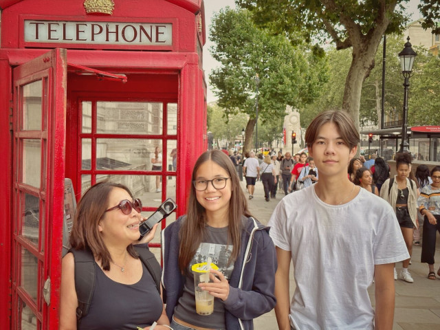 Wife and teenagers in front of a classic red London phone booth.