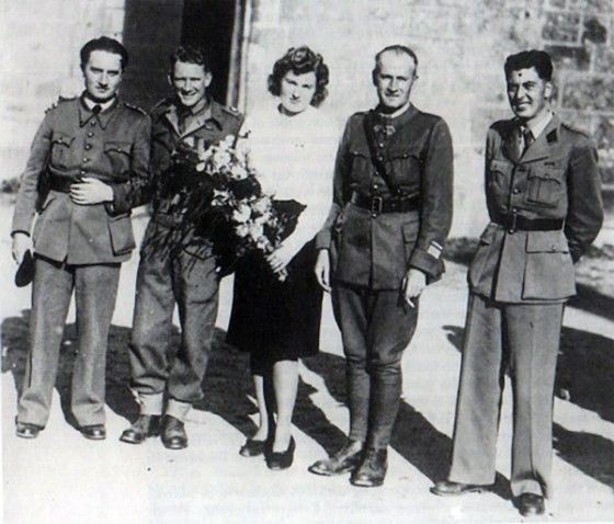 Maureen 'Paddy' O'Sullivan with four male officers in uniform. She's in civvies and holding flowers. They are all white.