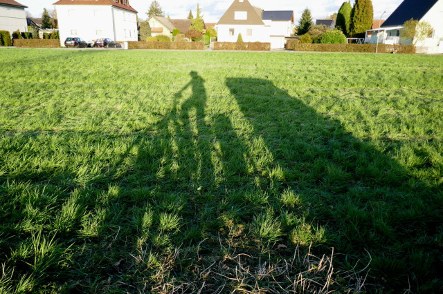 shadow of a bicycle with a small camper an a grassy field. Due to sunset the shadows appear unrealistically long