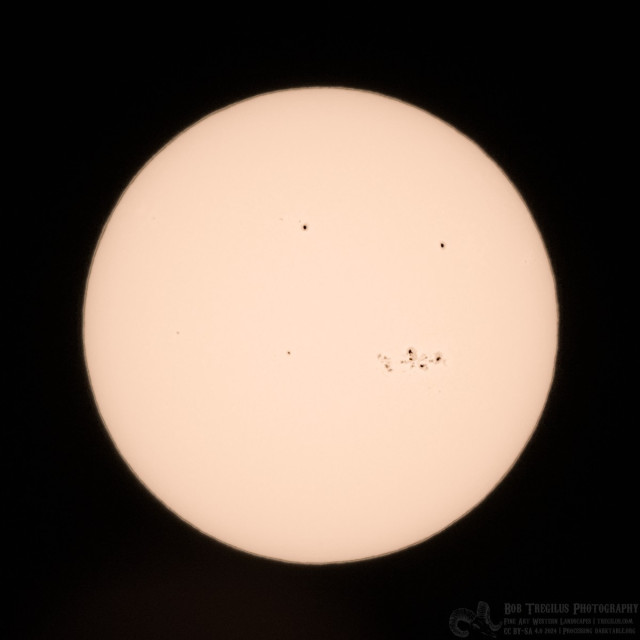 A photo of the sun. It's a yellow-white disk against a black background. There are five dark to black sunspot regions visible on the disk.