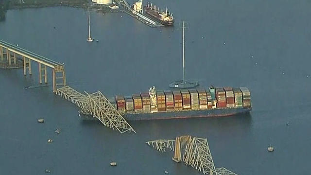 Aerial view of a bridge, which has collapsed over the front of a ship and elsewhere has completely collapsed