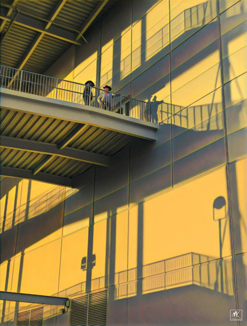  Color photo looking up at exterior metal framed entrance ramp and platform structures against a large stadium wall with two cowboy hat wearing persons standing on one of the platforms. The light from sunset is bathing the scene in yellow orange light and throwing sharply defined shadows of the metal structure and the cowboys against the wall. 