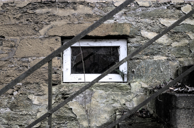 Ein Fenster in einer Steinmauer. Davor eine Steintreppe mit Treppengeländer