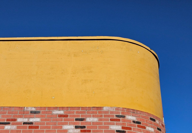 Upwards view of a curved corner at the top of a building painted a brilliant shade of mustard yellow beneath an equally brilliant blue sky. No filters nor color manipulation - exactly as the building appears on San Jose Boulevard approaching San Marco neighborhood.