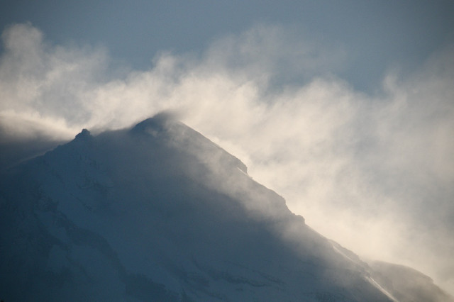 Snow-covered mountain peak with clouds of snow billowing from its slopes.