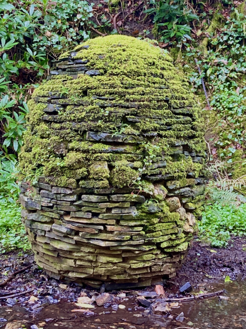 An egg shaped slate sculpture partially covered in moss.