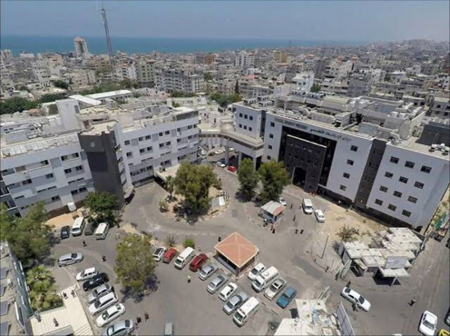 Aerial view of buildings of the Al Shifa medical complex in Gaza intact and in good functioning condition, with next to it a car park and trees.