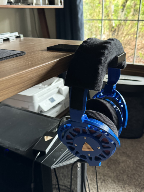 Ploopy headphones hanging from a hook that extends from the front of a desk.