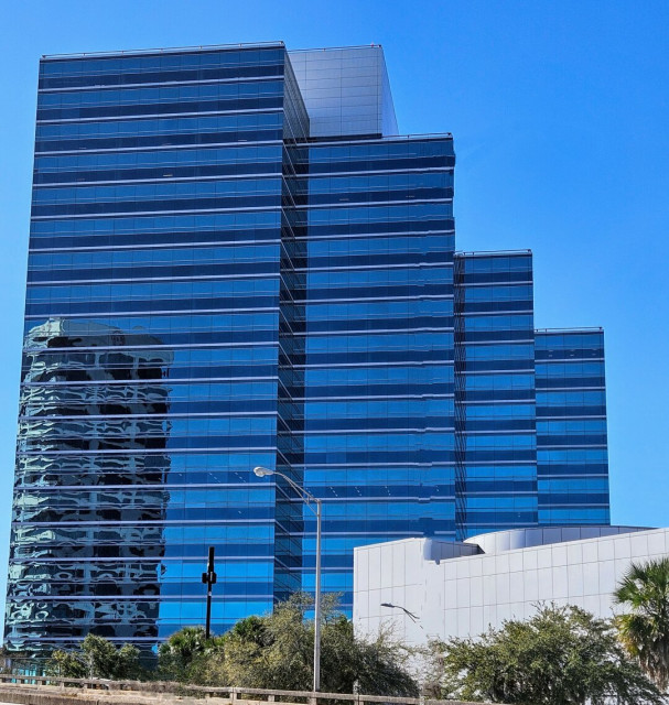 Large office building with interconnected stair like sections all completely covered with mirror like glass windows reflecting back the brilliant clear blue sky and nearby buildings.