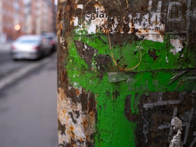 Remains of graffiti and posters on a pole. A car very out of focus.
