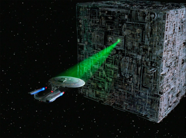 A Borg cube with a green beam locked on the starship Enterprise.