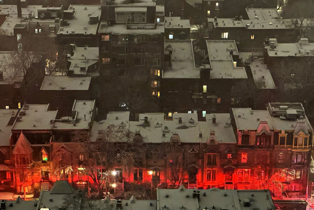 Overview of several streets of buildings at night, rooftops white with snow, and one row of buildings glowing red.