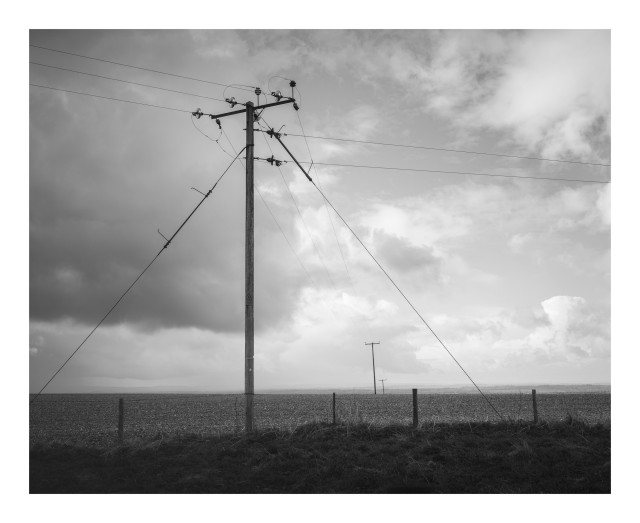 A black and white image of pylons in the middle of a rural landscape.