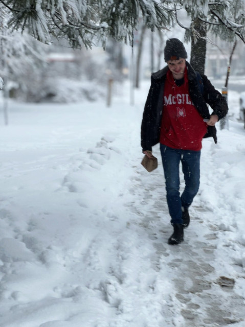 Guy in red sweatshirt with McGill logo on it walking on snow covered sidewalk.