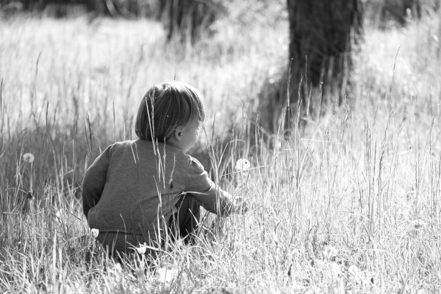 A black and white image of a young child sitting in a grassy field.