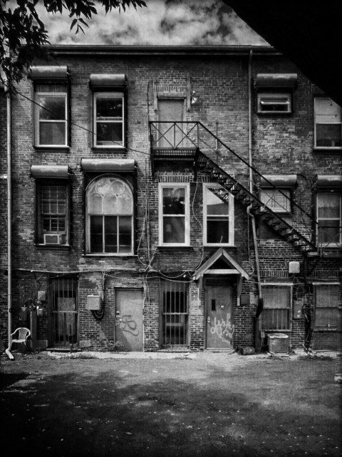 The back of a large brick building is covered with many windows of different shapes and sizes in this black and white image.