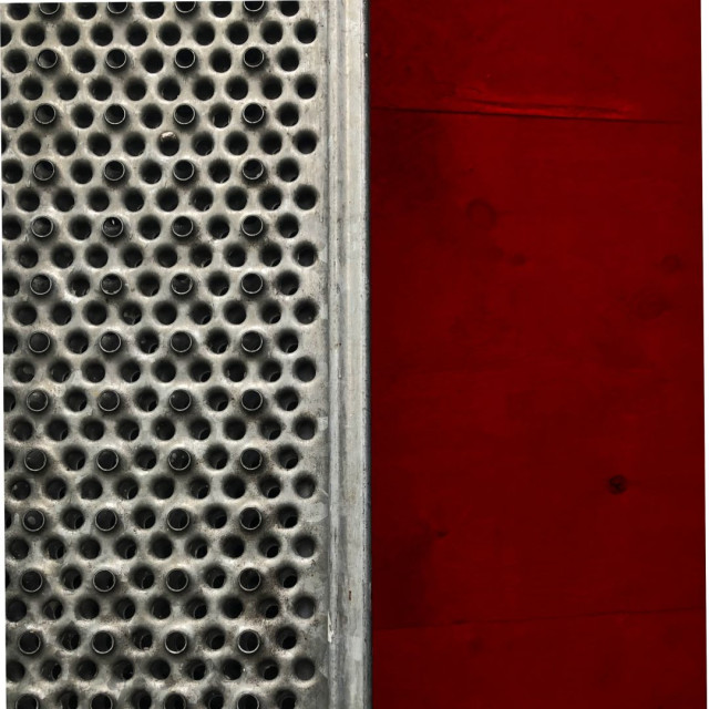 The left half of the image shows a detail of a metal grate while the right side shows a plywood surface painted red.