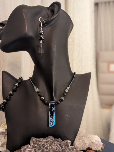 Photo of blue black agate gemstone pendant with black and Hematite styled beads and shimmering black beaded bracelet and earrings with grey pillar pendants and garnet gemstones