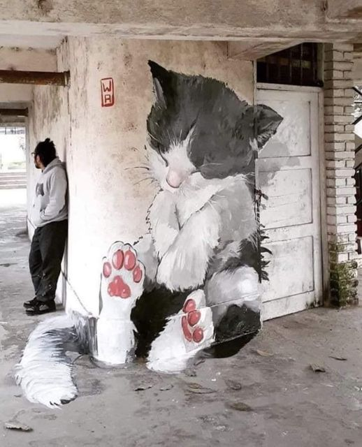 A painting done on the floor and wall and door of a part of building, making it seem like a huge cute kitty is resting there