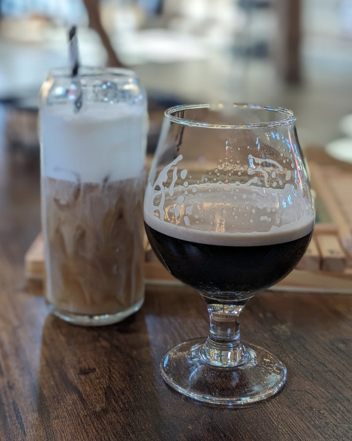 Left: An iced coffee in a glass. Tan in color with white cream. Paper straw.
Right: Black beer in a glass snifter.
Behind: Wooden Shut the Box game.