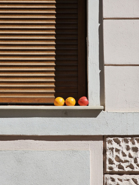 Image of an window still with two oranges and one apple on it, with sun shades.