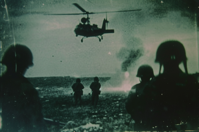 A helicopter hovering above a flare-marked landing zone, with infantry waiting to be extracted