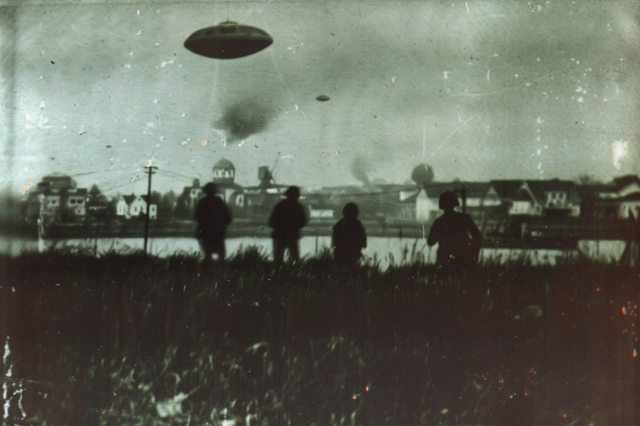 Flying saucers over a small town by a river, watched by a group of soldiers