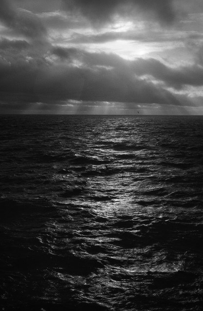 Monochrome image of a rough sea under a cloudy sky with light rays breaking through the clouds. Ilford FP4, Ilford DDX, Minolta X700.
