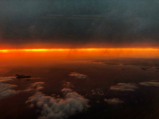 Aerial view of clouds with a vivid orange and red sunset on the horizon.