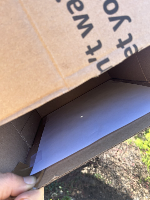 Photograph of a cardboard box that is completely sealed except for a 3 inch strip along one edge. When you Pierre inside the open area, you see a piece of white paper taped to the flat inner surface, and in the center of that piece of paper, a small glowing dot, which is a reflected image of the sun