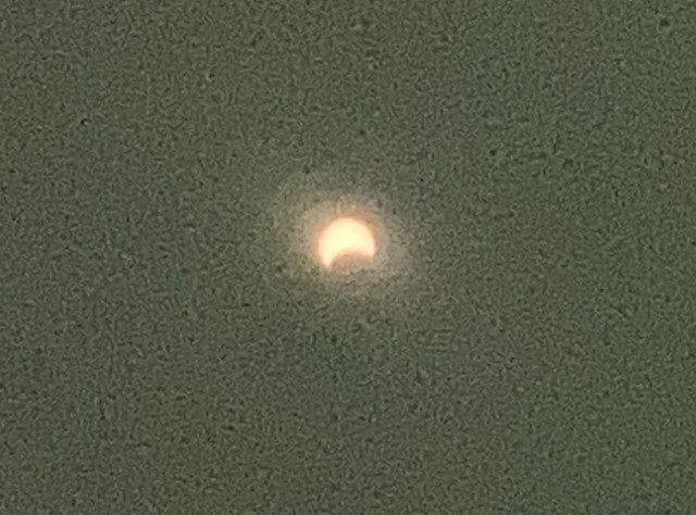 Blurry photo (taken with a phone through the special glasses) of the sun starting to be hidden by the moon from its bottom