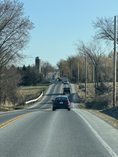 A line of vehicles on the road ahead of us. You can see a silo on the side of the road in the distance. There are a lot of silos around here.
