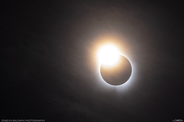Very glowy diamond ring at the edge of the eclipse, with a rainbow-like halo forming around the thin clouds.
