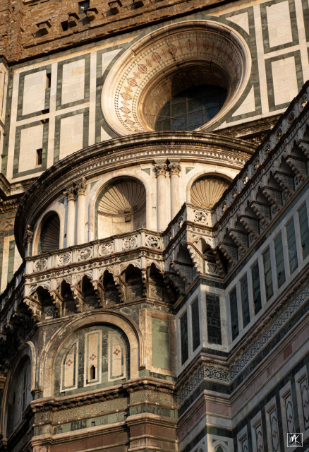 Color photo looking up at the side of the Duomo (Cathedral of Santa Maria del Fiore) in Florence, Italy showing the decorative architectural detail including a large round window. 
