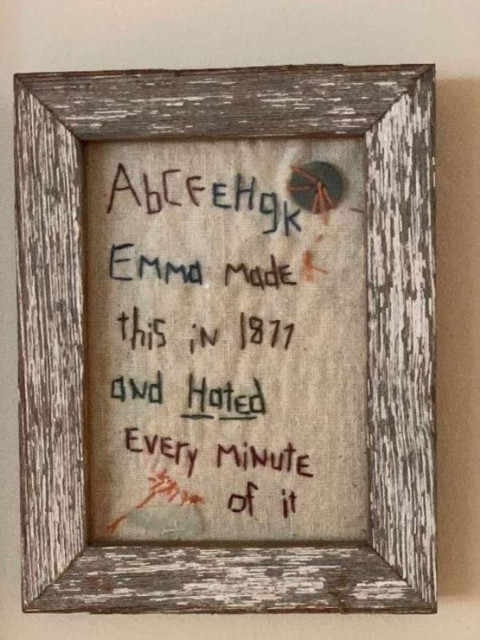 Sloppily embroidered piece in a weathered frame with partial alphabet letters and text reading "Emma made this in 1877 and Hated Every Minute of it."