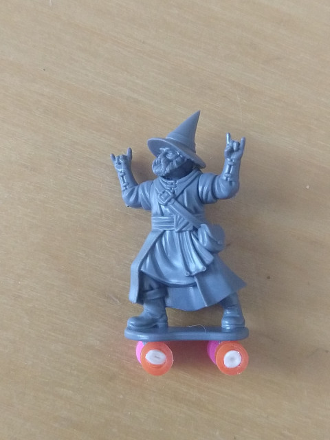 Same body, now with a bearded head with pointy Wizard hat, arms throwing devil horns and the base has been nodded to look like a skate board.