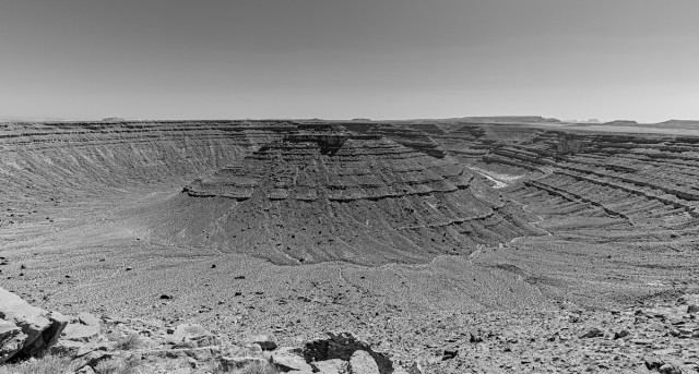 Black and white photo of a deep circular canyon. A river can be seen in the bottom of the canyon on the right. The circular area is where the river once ran but later was cutoff and now flows behind and large circular bluff in the center.