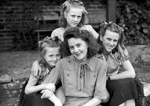 Odette Samsom with her three daughters before the war. She is a white woman with dark hair and is sat in a garden chair, with the three girls around her.