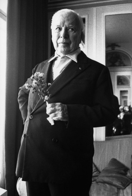 Chaplin is indoors at daytime while holding some flowers. He is dressing a dark suit. 