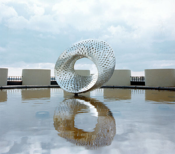 “The Mobius Strip” is a sculpture by Wilson that consists of several reflective steel strips welded onto a circular tube. Their orientation shifts around the tube to produce a visual effect similar to a one-sided Mobius strip.