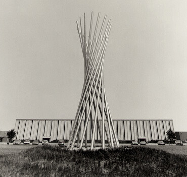 Wilson’s “Tractricious” consists of sixteen long steel tubes. Each one is straight, but they lean together to form a curved hyperboloid shape.