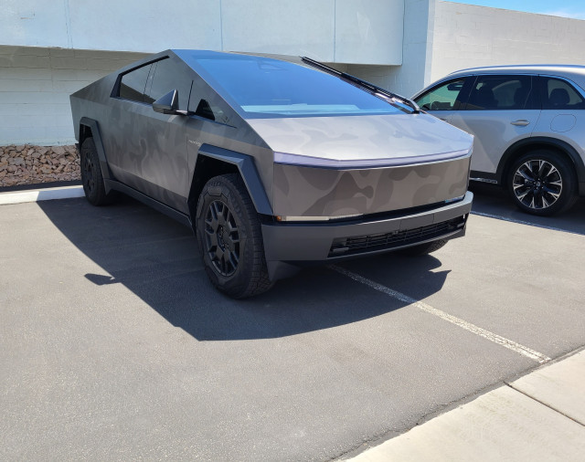 Photo of a Tesla Cybertruck painted in a four-toned gray camouflage scheme, straddling two parking spaces.