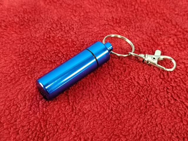 A blue powder-coated aluminum pill box keychain.

What use is this?