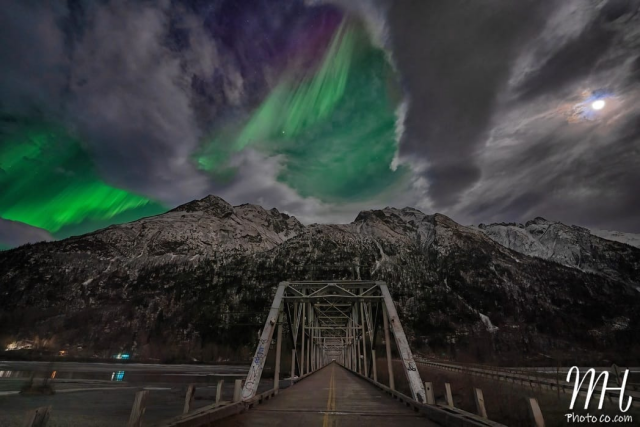 Northern Lights in bright shades of green with some clouds mixed in as seen from one side of the Knik River Bridge overlooking Pioneer Peak.